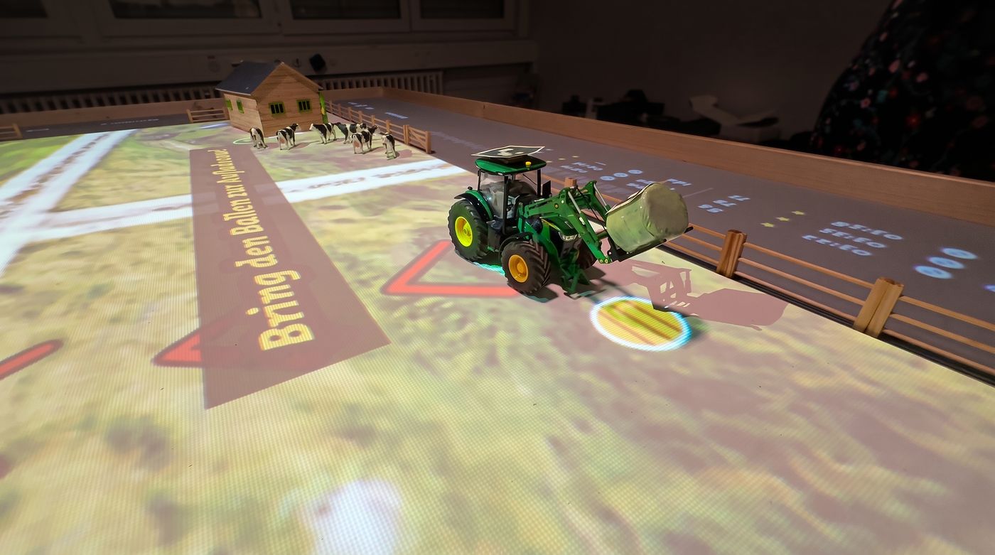 Insel 1: Traktor mit Frontlader und Heuballen, projizierter Auftrag «Bring den Ballen»